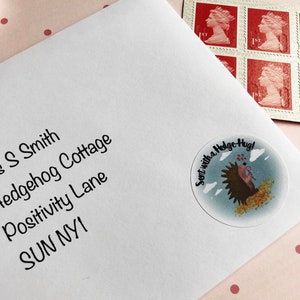 May include: White envelope with address and a round sticker that says "Sent with a Hedge Hug!" featuring a hedgehog illustration. Red postage stamps with a profile of Queen Elizabeth II are in the upper right corner.