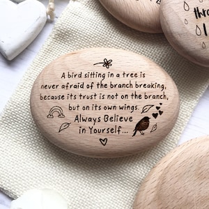 May include: Wooden engraved motivational quote on a small oval shaped piece of wood. The quote reads "A bird sitting in a tree is never afraid of the branch breaking, because its trust is not on the branch, but on its own wings. Always Believe in Yourself..."