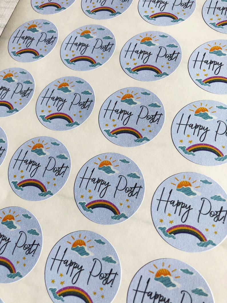 以下が含まれることがあります： 水色の背景に「Happy Post!」の文字が筆記体で書かれた丸いステッカーのシート。虹、太陽、雲、星のイラストも描かれています。