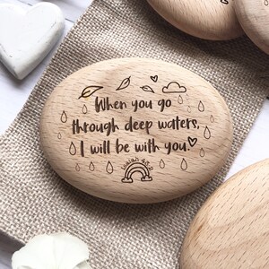 Puede incluir: Ficha de madera ovalada con una ilustraci&oacute;n dibujada a mano de un arco&iacute;ris, gotas de lluvia y hojas. El texto dice "When you go through deep waters, I will be with you." e "Isaiah 43:2".