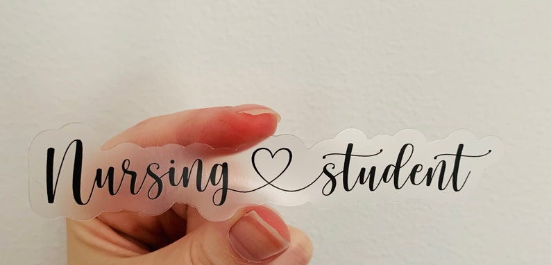 K&ouml;nnte beinhalten: Ein transparenter Aufkleber mit dem Text "Nursing &hearts; student" in schwarzer Kursivschrift.