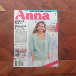 以下が含まれることがあります： 編み物と針仕事のマガジン、アンナの雑誌の表紙です。表紙には、薄い青色のニットカーディガンと白いスカートを着た女性が写っています。雑誌のタイトルはピンクと白の文字で書かれています。表紙には、ボビンレースのパターン、ニードルポイントとクロスステッチのデザイン、円形のクロシェのプレースマットなど、さまざまな編み物とクロシェのプロジェクトが掲載されています。