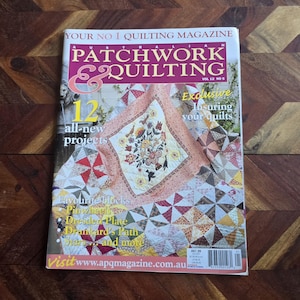 May include: A copy of "Patchwork & Quilting" magazine, showcasing a quilt with floral and bird motifs on its cover. The magazine's cover also advertises new projects and quilting techniques. The magazine is placed on a wooden surface.
