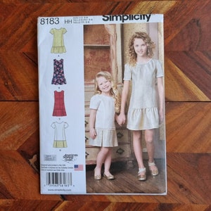 May include: Simplicity sewing pattern number 8183 for girls' dresses in sizes 3-6. The pattern includes four different styles: a yellow dress with a ruffle, a floral print dress, a plaid dress, and a dress with a yellow and white striped bottom. The pattern is designed and printed in the USA.