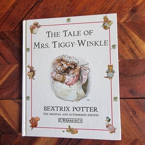 May include: The Tale of Mrs. Tiggy-Winkle book cover featuring a hedgehog wearing a pink and white dress and apron. The book is by Beatrix Potter and is the original and authorised edition published by F. Warne & Co.