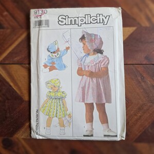 May include: A Simplicity sewing pattern envelope, number 9130, size 2, featuring illustrations of children wearing dresses and bonnets. The cover displays three distinct garment designs with floral details, short puff sleeves, and collars, presented on a white background with black text and line drawings.