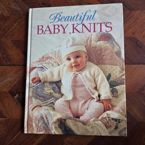May include: A book titled "Beautiful Baby Knits" with a photo of a baby wearing a white knitted cardigan and a white knitted hat on the cover.