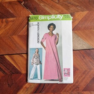 Peut inclure: Patron de couture Simplicity numéro 1970 pour une robe maxi avec une fente à l'avant. Le patron comprend un transfert pour broderie. Le mannequin porte une robe rose avec un motif brodé blanc sur la manche.