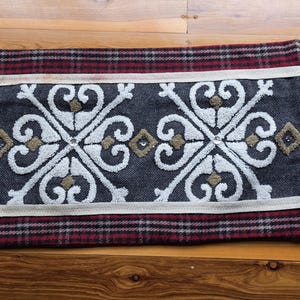 May include: A rectangular pillow cover featuring a dark gray herringbone center with white embroidered scrollwork and tan diamond accents. The top and bottom edges have red and black plaid borders with cream trim and faux fur side fringe.