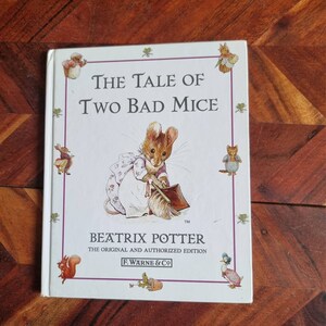 May include: A white book cover featuring an illustration of a mouse holding a dustpan and brush. The title is "The Tale of Two Bad Mice" by Beatrix Potter. The book is the original and authorised edition published by F. Warne & Co.