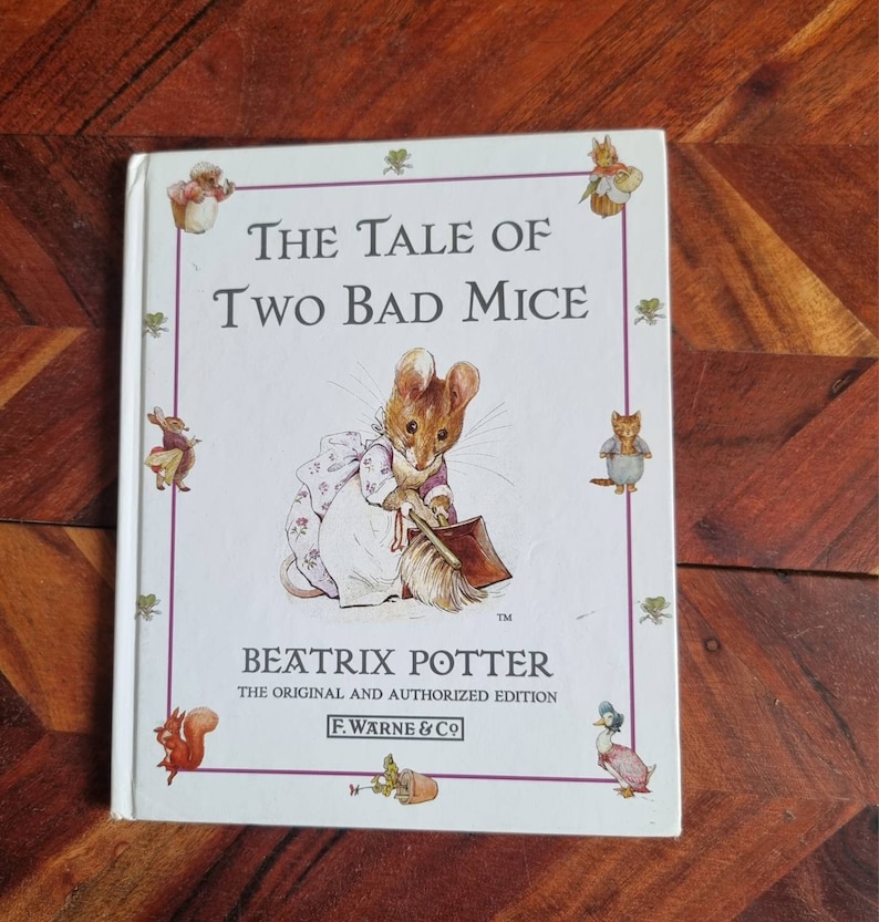 May include: A white book cover featuring an illustration of a mouse holding a dustpan and brush. The title is "The Tale of Two Bad Mice" by Beatrix Potter. The book is the original and authorised edition published by F. Warne & Co.