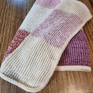 Puede incluir: Una manta de punto con un patrón de cuadros en tonos beige, rosa y rojo.
