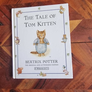 May include: A white book cover featuring a blue and orange illustration of a kitten wearing a blue shirt. The title of the book is "The Tale of Tom Kitten" by Beatrix Potter. It is the original and authorised edition published by F. Warne & Co.