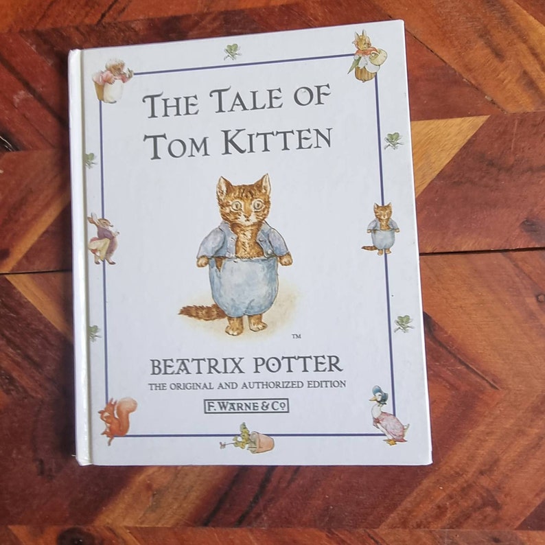 May include: A white book cover featuring a blue and orange illustration of a kitten wearing a blue shirt. The title of the book is "The Tale of Tom Kitten" by Beatrix Potter. It is the original and authorised edition published by F. Warne & Co.