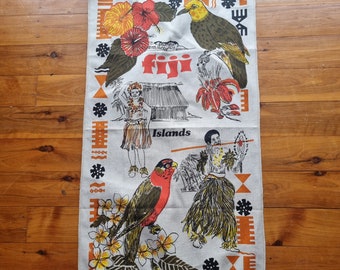 Op de afbeelding: Een witte linnen theedoek met een kleurrijk ontwerp met een vogel, bloemen en mensen. De tekst "Fiji Islands" is op de handdoek gedrukt.