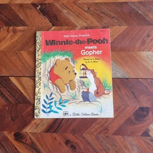 Könnte beinhalten: Ein Vintage-Buch der Little Golden Book-Reihe mit Winnie Puuh und Gopher. Das Cover zeigt Winnie Puuh, der traurig aussieht, und Gopher, der eine Laterne hält. Der Titel des Buches lautet "Winnie Puuh trifft Gopher".