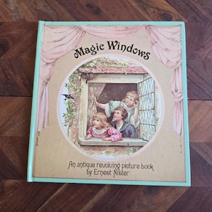 May include: A vintage children's book titled "Magic Windows: An antique revolving picture book by Ernest Nister". The cover features a colourful illustration of three children looking out of a window.