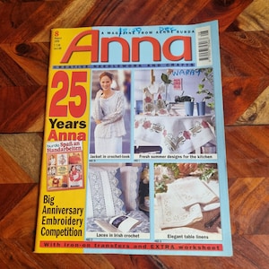 Op de afbeelding: Een tijdschriftcover voor Anna, een creatief naai- en handwerktijdschrift. De cover toont een vrouw die een wit gebreid jasje draagt, een tafelsetting met geborduurde tafelkleden en de tekst "25 jaar Anna".