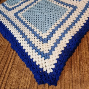 May include: A crocheted baby blanket with a blue and white diamond pattern and a blue border.
