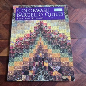 May include: A book titled "Colorwash Bargello Quilts" by Beth Ann Williams. The cover features a colorful quilt design with a geometric pattern in shades of yellow, brown, green, and red. The book is on a dark wood surface.