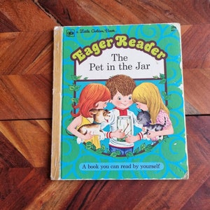 May include: A Little Golden Book titled "Eager Reader: The Pet in the Jar". The cover features three children looking into a jar with a bug inside. The book is on a wooden surface.