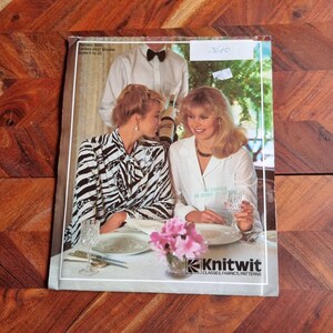 Puede incluir: Dos mujeres están sentadas en una mesa en un restaurante. Una mujer lleva una blusa a rayas blancas y negras, mientras que la otra lleva una blusa blanca. Ambas sostienen copas de vino. La mesa está puesta con un mantel blanco, cubiertos y un jarrón de flores rosas. El texto "Knitwit Classes Fabrics Patterns" es visible en la parte inferior de la imagen.