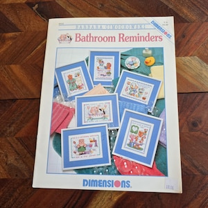 Puede incluir: Un folleto de patrones de punto de cruz titulado "Bathroom Reminders" de Barbara Cimochowski. El folleto presenta siete patrones de punto de cruz coloridos con lindas ilustraciones de animales y refranes sobre el tema del baño. El folleto es publicado por Dimensions.