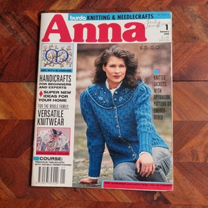 Op de afbeelding: Een tijdschriftcover voor Anna, een brei- en handwerkmagazine. De cover toont een vrouw die een blauwe gebreide jas draagt met geborduurde details. De titel van het tijdschrift is in rood en wit. De cover bevat ook de tekst "Handicrafts for Beginners and Experts", "Super New Ideas for Your Home", "Versatile Knitwear", en "Knitted Jackets, with Openwork Pattern or Embroidered".