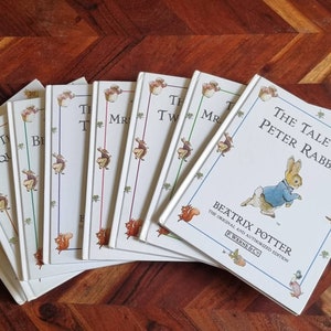 May include: A collection of eight vintage children's books featuring Beatrix Potter characters. The books are in white covers with colourful illustrations and titles like "The Tale of Peter Rabbit", "The Tale of Squirrel Nutkin", "The Tale of Mr. Tod", and "The Tale of Two Bad Mice".