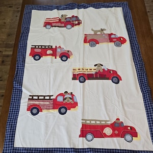 May include: A white and blue checked fabric baby blanket with red fire engines and dogs embroidered on it.