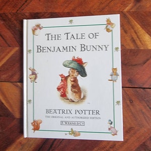 May include: A white book cover with a green border featuring a cartoon rabbit wearing a green hat and red scarf. The title is "The Tale of Benjamin Bunny" by Beatrix Potter. The book is the original and authorised edition published by F. Warne & Co.