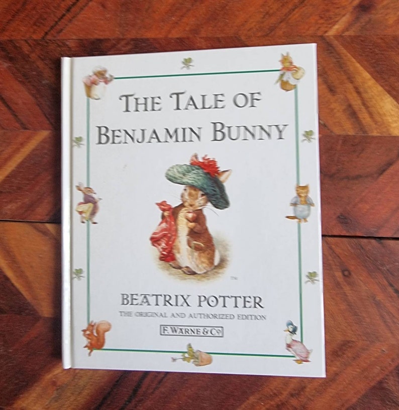 May include: A white book cover with a green border featuring a cartoon rabbit wearing a green hat and red scarf. The title is "The Tale of Benjamin Bunny" by Beatrix Potter. The book is the original and authorised edition published by F. Warne & Co.