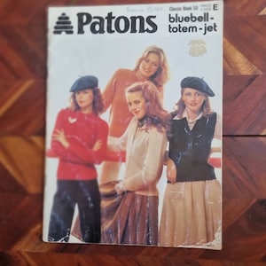 May include: A Patons yarn catalogue cover featuring four women wearing different sweaters and hats. The catalogue is titled "Classic Book 53" and the price code is "E". The catalogue is for "bluebell-totem-jet" yarn.