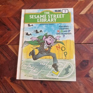 May include: A Sesame Street Library book featuring the letters N, O, and P, and the number 7. The cover features Count von Count dressed as a vampire running through a hopscotch game. The book is volume 7 of the Sesame Street Library series.