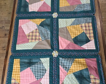 May include: A set of four quilted placemats with a patchwork design. The placemats are made of green, pink, yellow, and brown fabric. Each placemat has a different pattern, but they all have a similar color scheme.