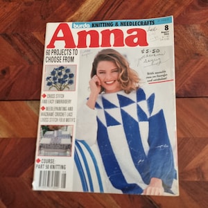 Op de afbeelding: Een tijdschriftcover voor Anna, een brei- en handwerkmagazine. De cover toont een vrouw die een blauwe en witte gebreide trui draagt met een geometrisch patroon. De titel van het tijdschrift is in rode en witte letters. De cover bevat ook de tekst "60 projecten om uit te kiezen" en "€ 5,50".