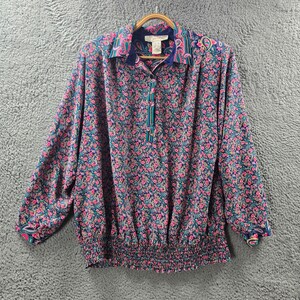 Könnte beinhalten: Eine langärmelige, blaue Seidenbluse mit Blumenmuster. Die Bluse hat einen elastischen Bund und einen Kragen mit Paisley-Muster.