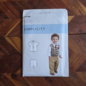 May include: A Simplicity sewing pattern for a boy's outfit, including a shirt, shorts, vest, and trousers. The pattern features a photo of a young child wearing the outfit. The pattern is labelled "Easy-to-Sew".
