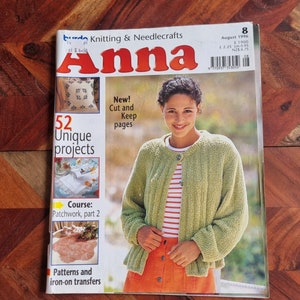 Op de afbeelding: Een tijdschriftcover voor Burda Breien & Handwerken Anna, augustus 1996 editie. De cover toont een vrouw die een groene cardigan en een oranje rok draagt. De titel van het tijdschrift is in rood en wit. De cover toont ook de tekst "52 unieke projecten" en "Nieuw! Knip uit en bewaar".