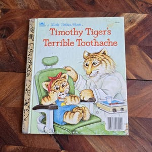 May include: A Little Golden Book titled "Timothy Tiger's Terrible Toothache" features an illustration of a tiger dentist examining a young tiger patient in a dentist's chair.