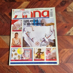 Op de afbeelding: Een tijdschriftcover met een witte tafelkleed met een blauw en wit kruissteekontwerp van zeilboten en een nautisch wiel. De titel van het tijdschrift is "Anna" en de tekst "Light and airy: 57 hits for summer" is vetgedrukt. Het tijdschrift gaat over handwerken en knutselen.