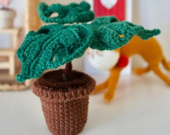 May include: A crocheted green plant with large leaves in a brown crocheted pot. The plant is sitting on a white surface.