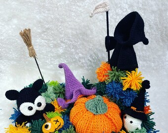 May include: A Halloween-themed crocheted scene with a black cat, a pumpkin, a ghost, and a grim reaper. The scene is surrounded by colorful pom-poms.