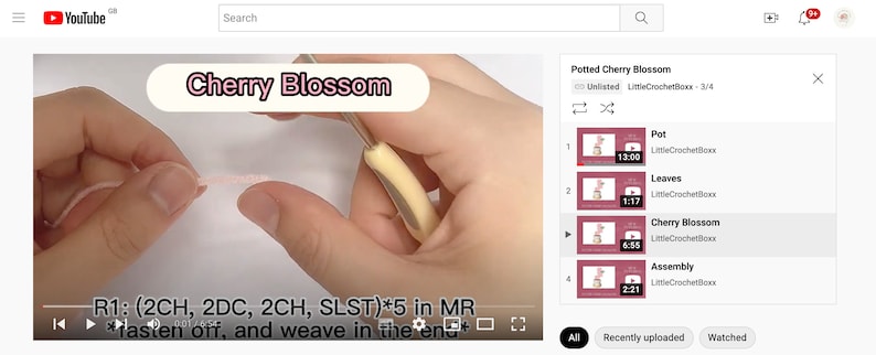 K&ouml;nnte beinhalten: Ein YouTube-Video mit dem Titel "Cherry Blossom" zeigt eine Nahaufnahme von H&auml;kelarbeiten. Das Video enth&auml;lt Textanweisungen und eine Liste verwandter Videos, darunter "Pot", "Leaves" und "Assembly".