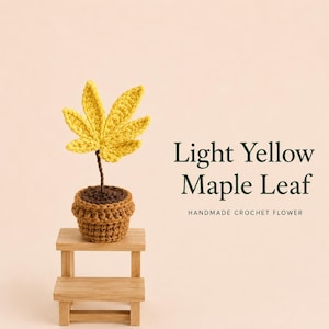 Pode incluir: Uma folha de ácer de croché amarelo-claro com um caule castanho, plantada num vaso de croché castanho. O texto "Light Yellow Maple Leaf" e "HANDMADE CROCHET FLOWER" está impresso à direita. A planta repousa sobre um pequeno banco de madeira.