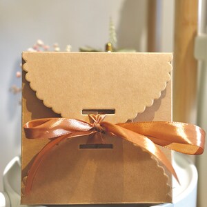 May include: A brown cardboard gift box with a scalloped edge and a brown satin ribbon tied in a bow.