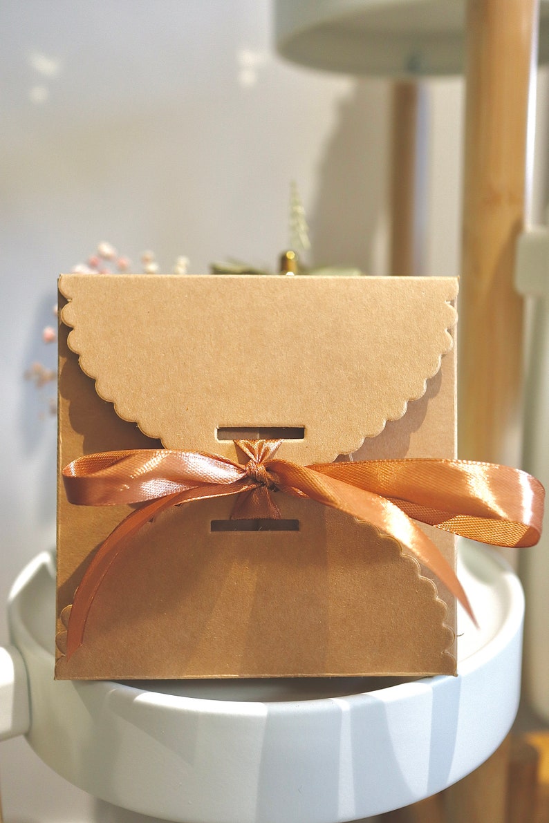 May include: A brown cardboard gift box with a scalloped edge and a brown satin ribbon tied in a bow.