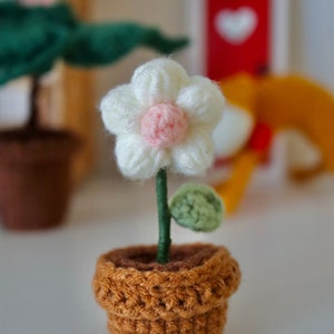 May include: A small crocheted flower in a brown pot. The flower is white with a pink center and has a green leaf.