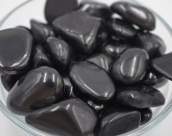 May include: A bowl filled with smooth, black tumbled stones. The stones are various shapes and sizes, with a glossy finish.
