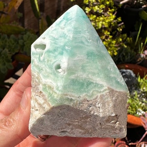 May include: A green and white celestite crystal point with a rough, natural base. The crystal has a layered, banded appearance and is a popular choice for crystal healing and meditation.